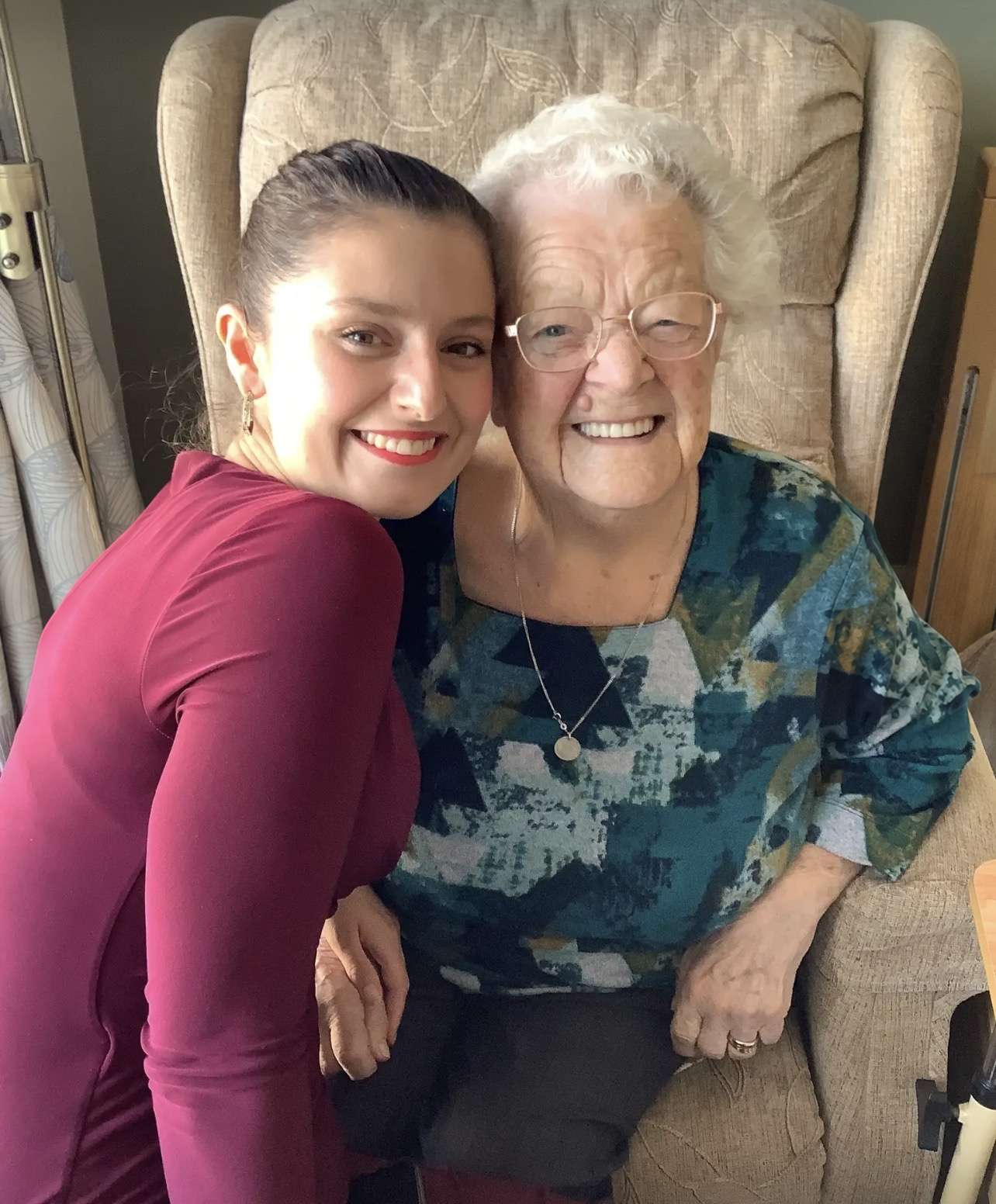 Shannon Kitchen smiling cheek to cheek with an elderly resident in a beige armchair